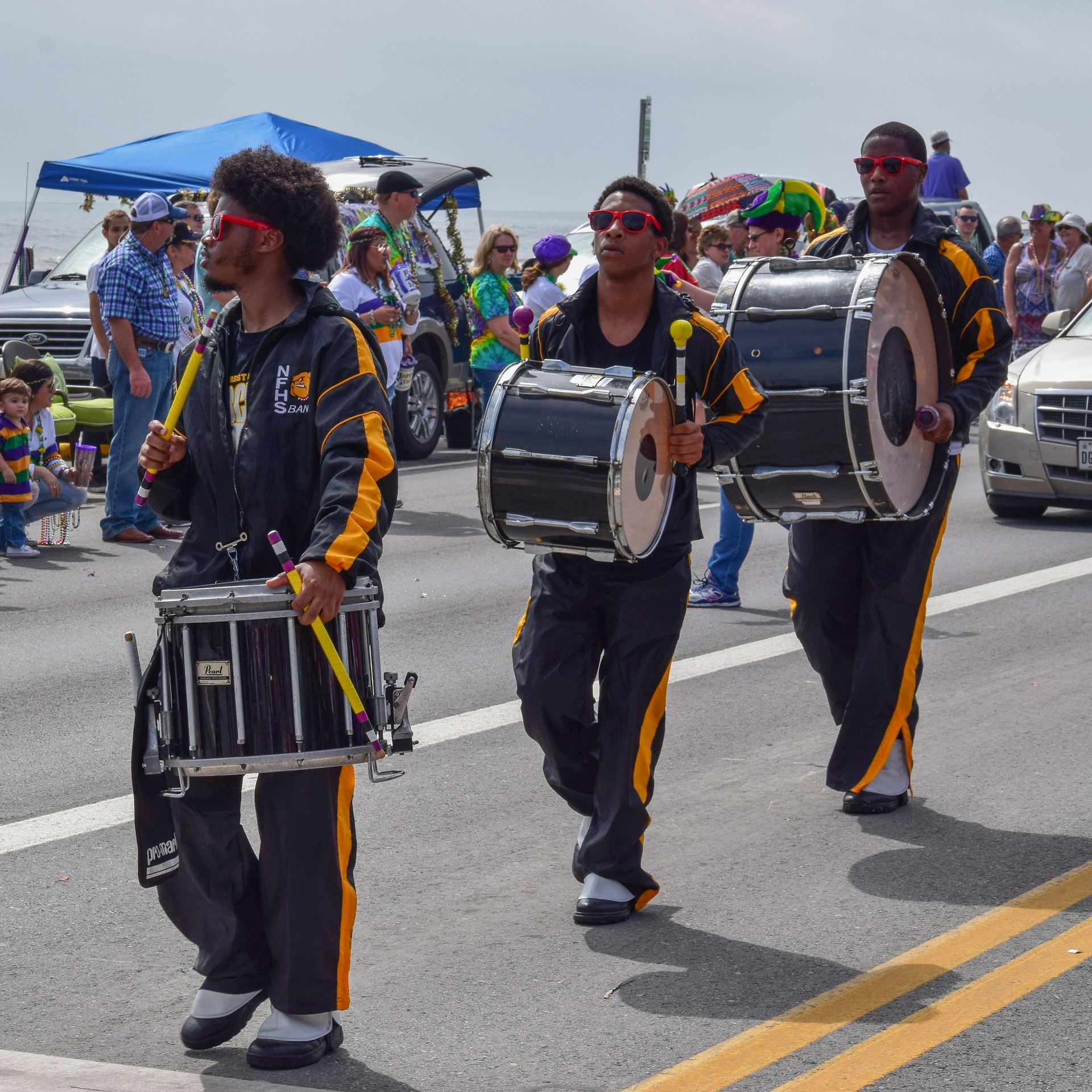 Three black men play drums as they walk along taking part in a parade down the street