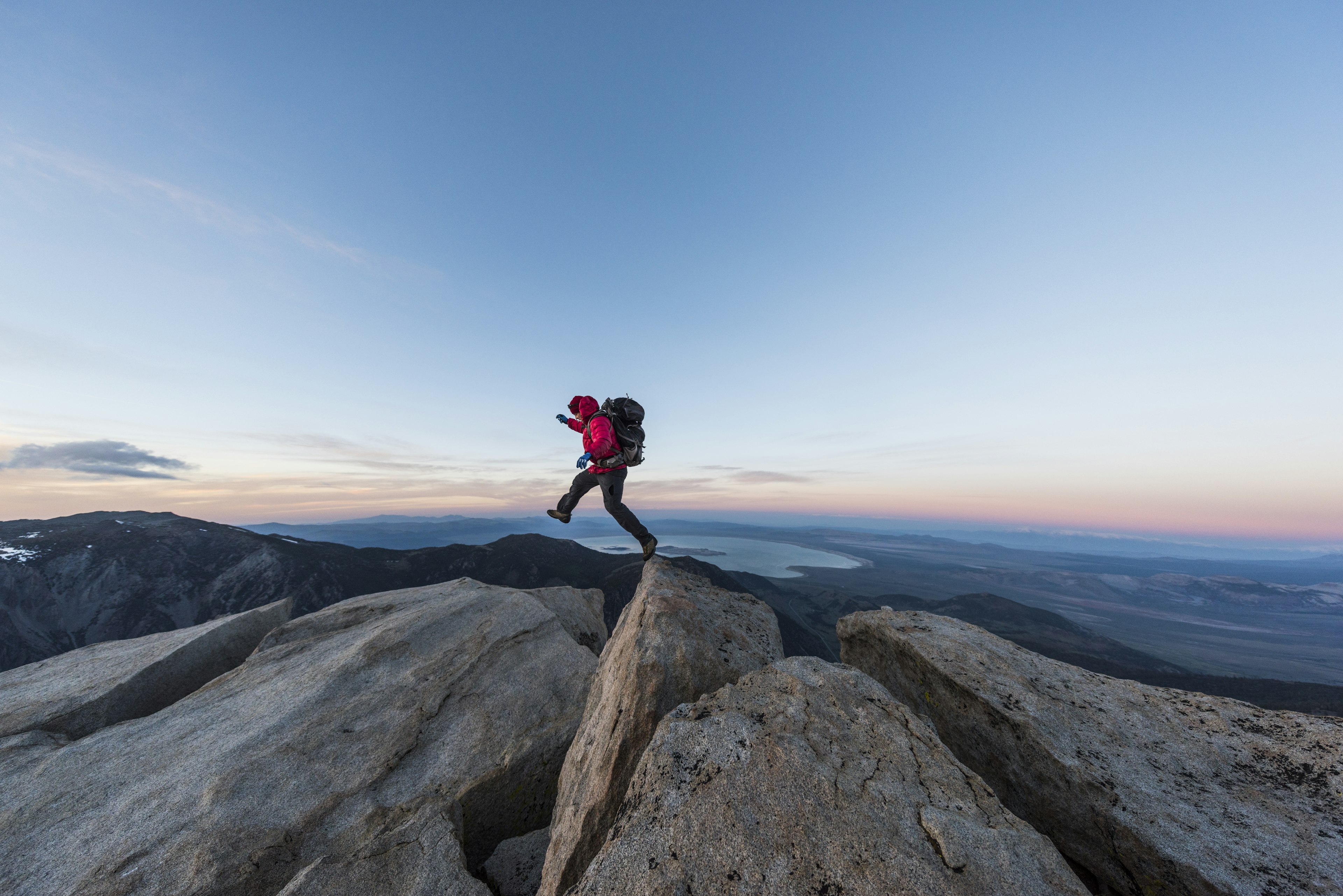 Strong mountain climber hiking and jumping on the summit ridge of a peak at sunset
