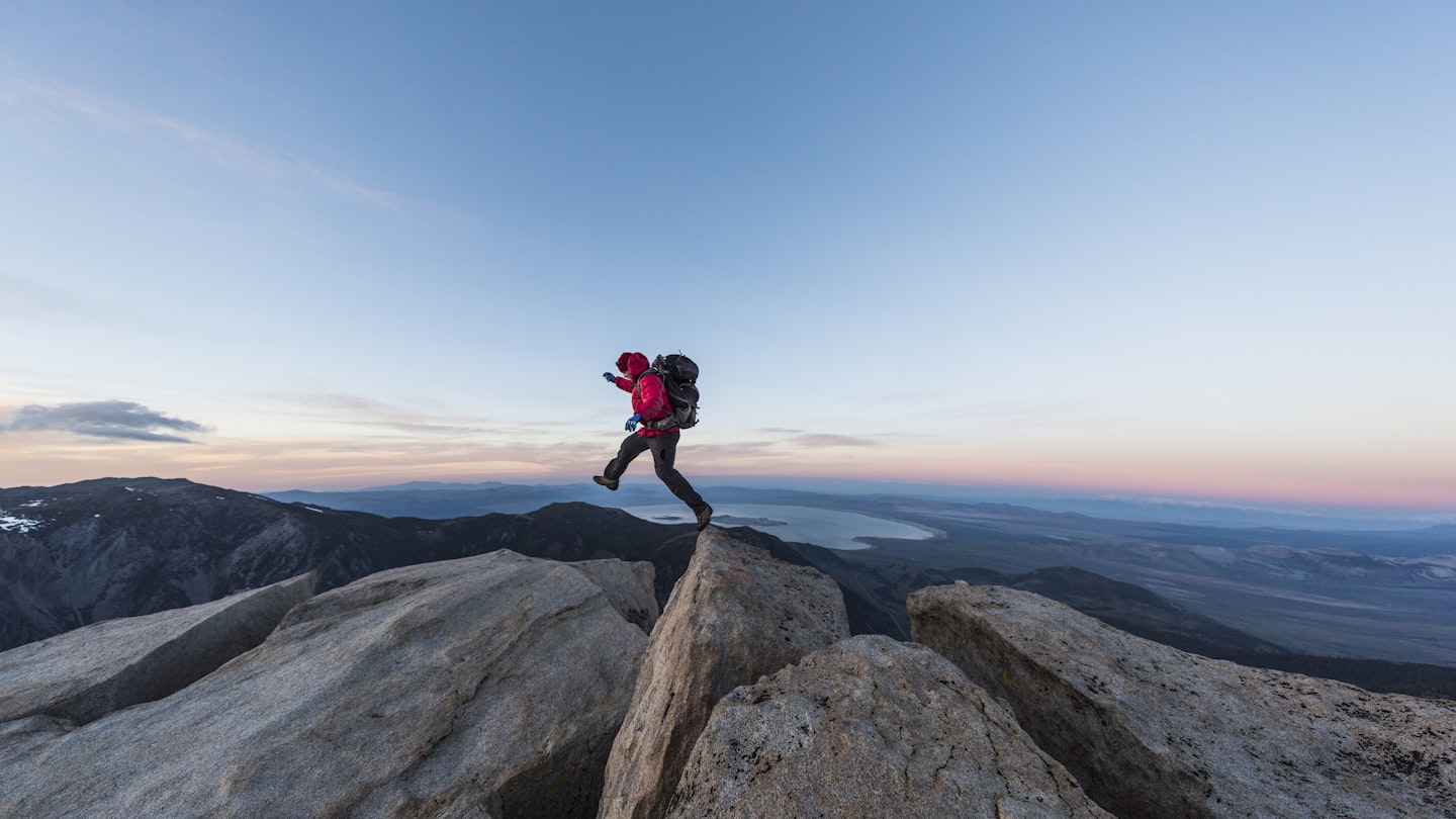 Strong mountain climber hiking and jumping on the summit ridge of a peak at sunset