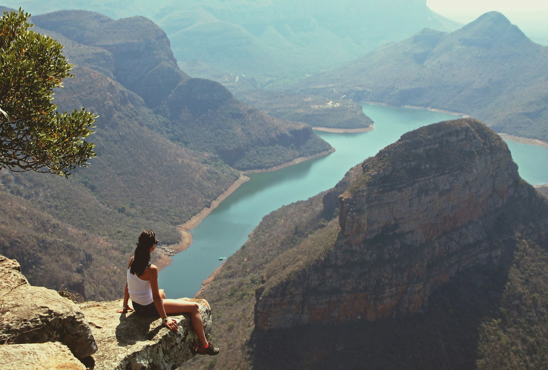 Woman sitting on a rock looking at a view of a deep canyon and river at Blyde River Canyon in South Africa