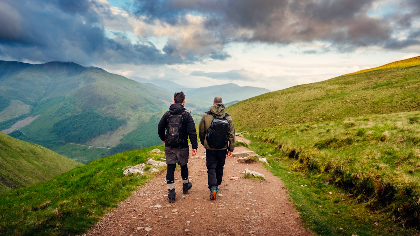 2 men pictured from the rear, walking along a hiking path on Ben Nevis in Scotland.