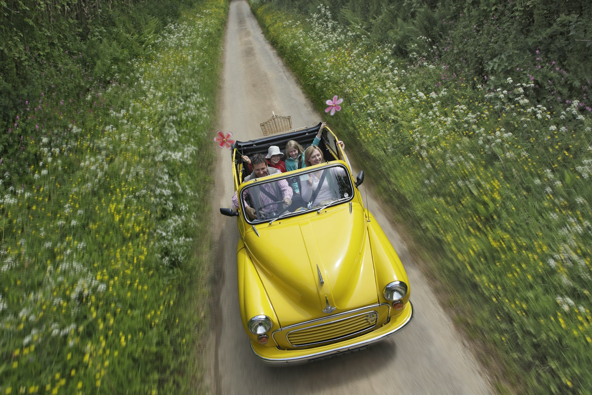 A family driving in open top car down country lane in England