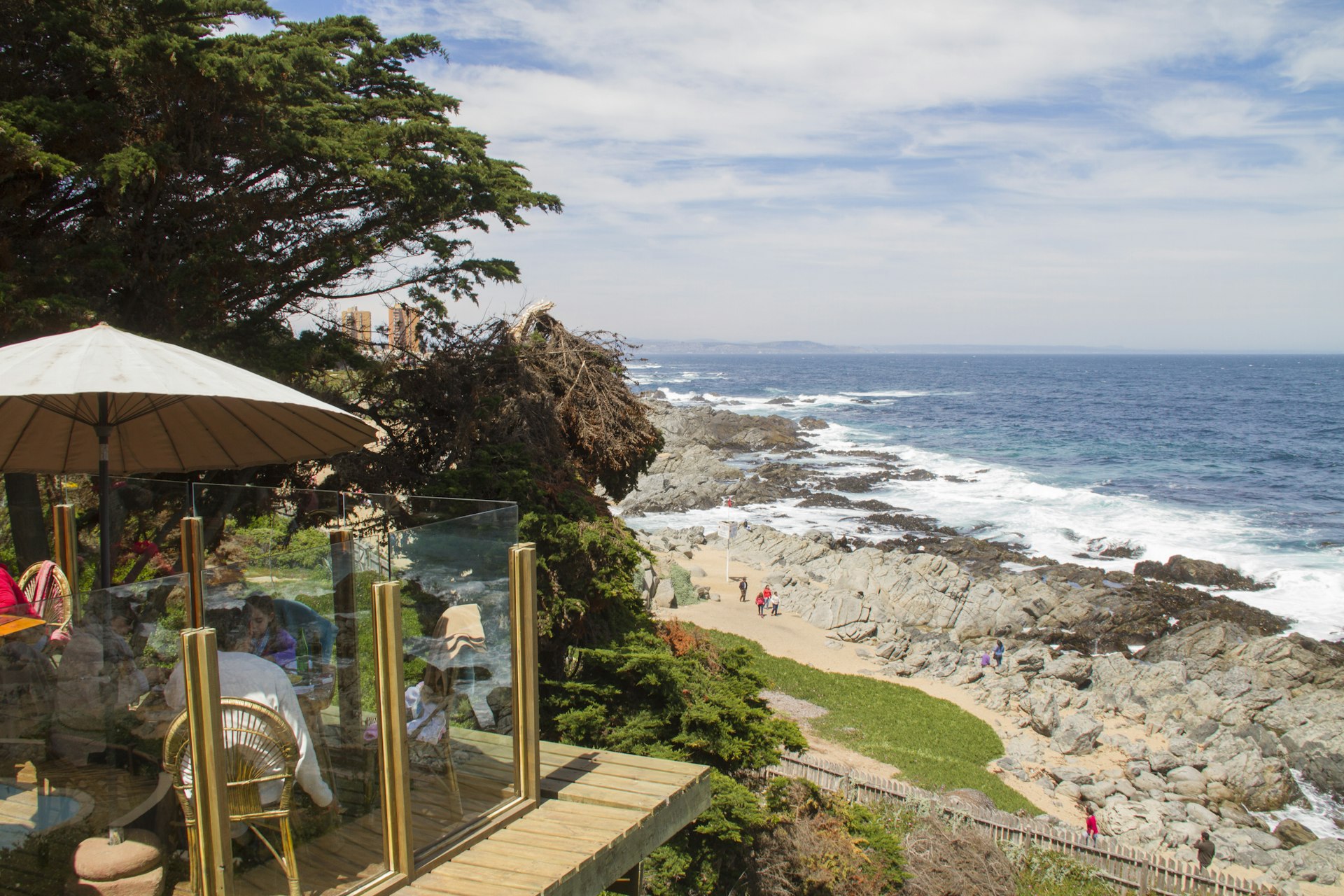 A family eats in a restaurant on a platform overlooking a sandy beach with some rocky sections on Isla Negra, Chile