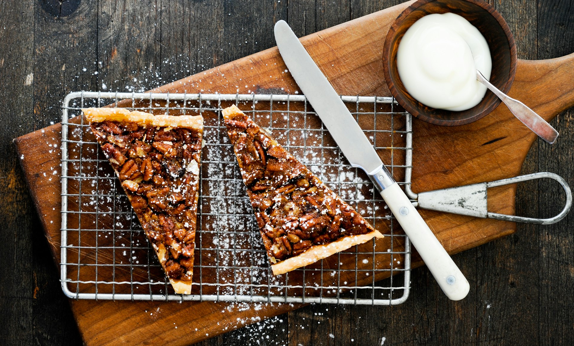 Small pecan tarts on a wooden cutting board with a knife and whipped cream