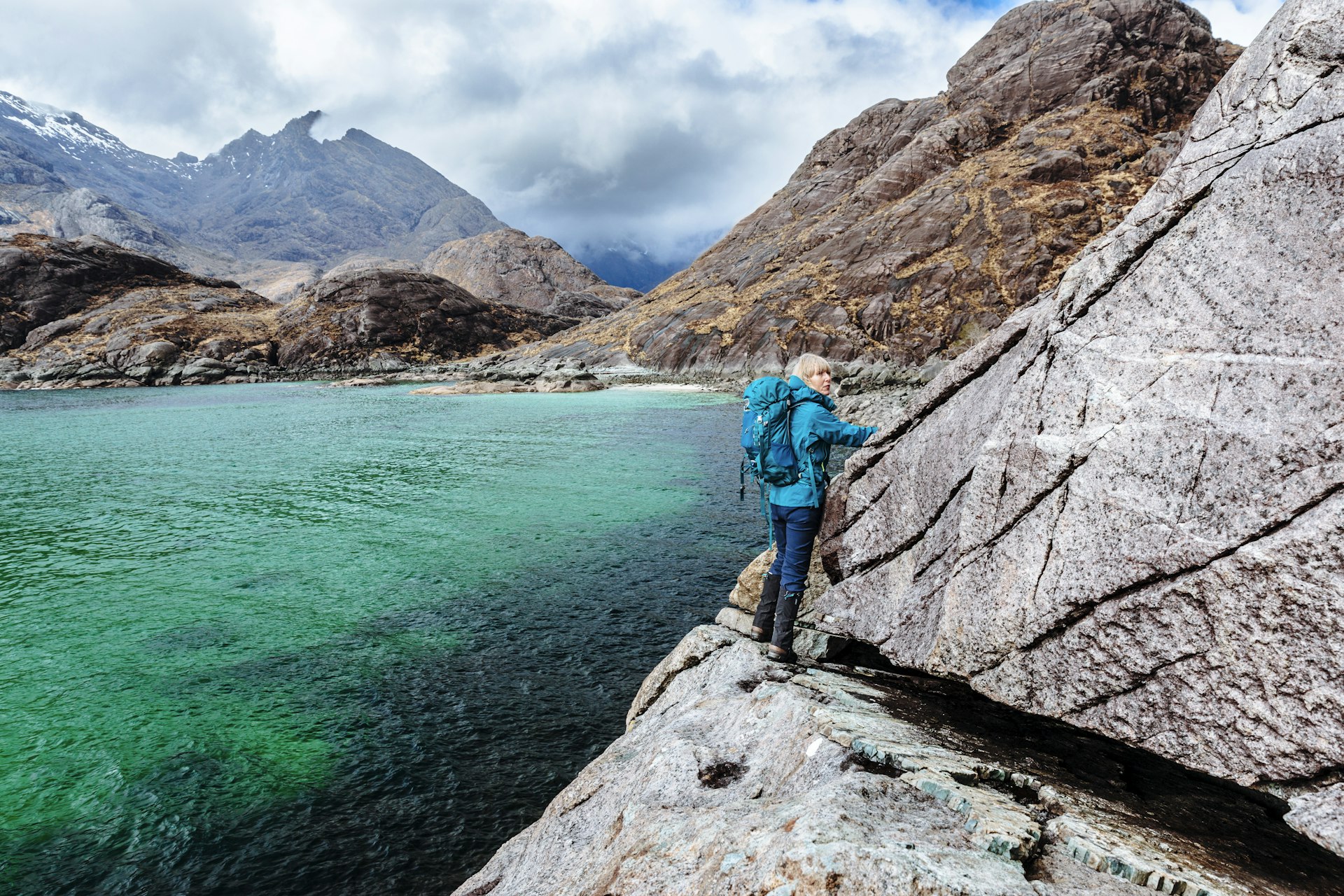 A woman hugging a tight path alongside some rocks above a lake