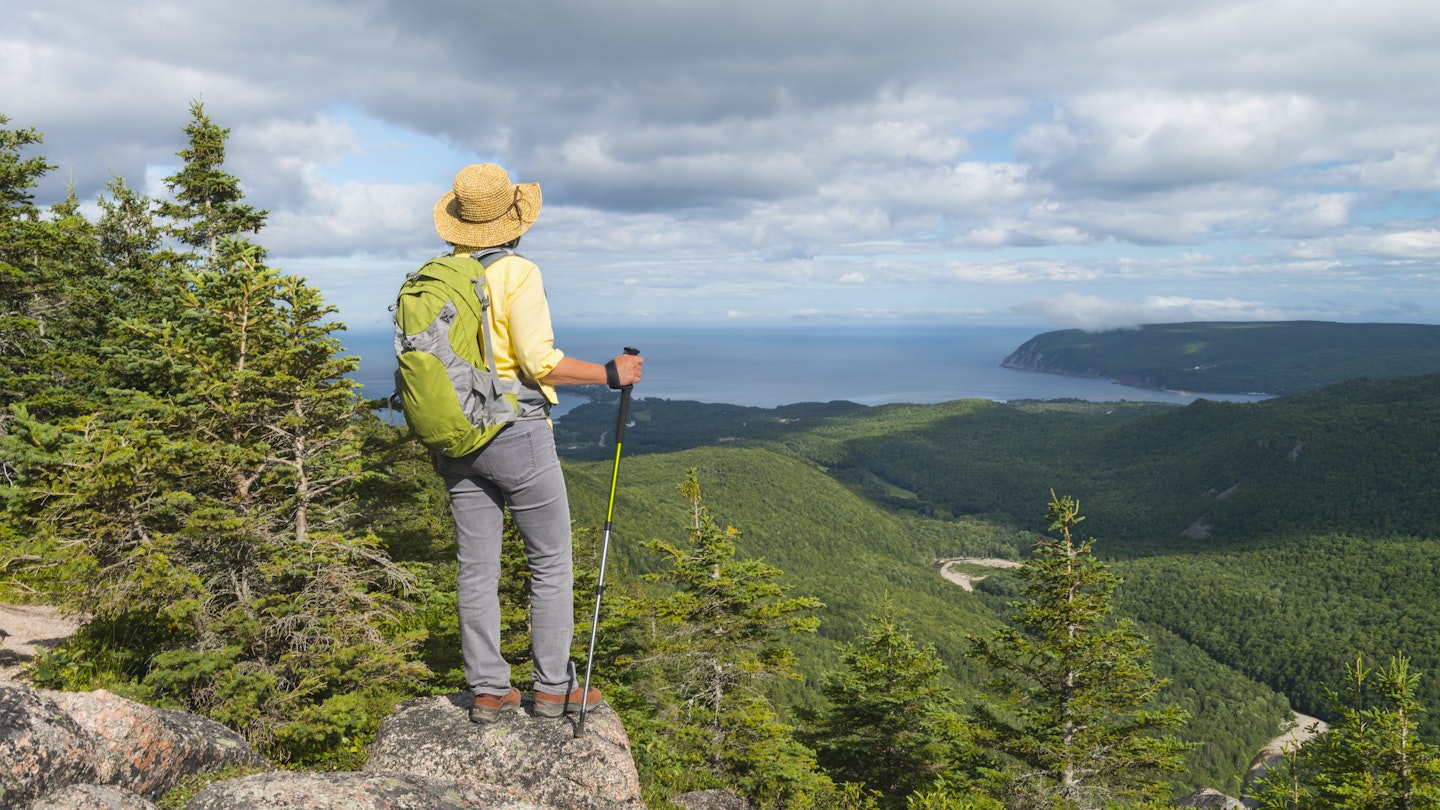 Female hiker standing at the top of a mountain in Cape Breton Highlands National Park.