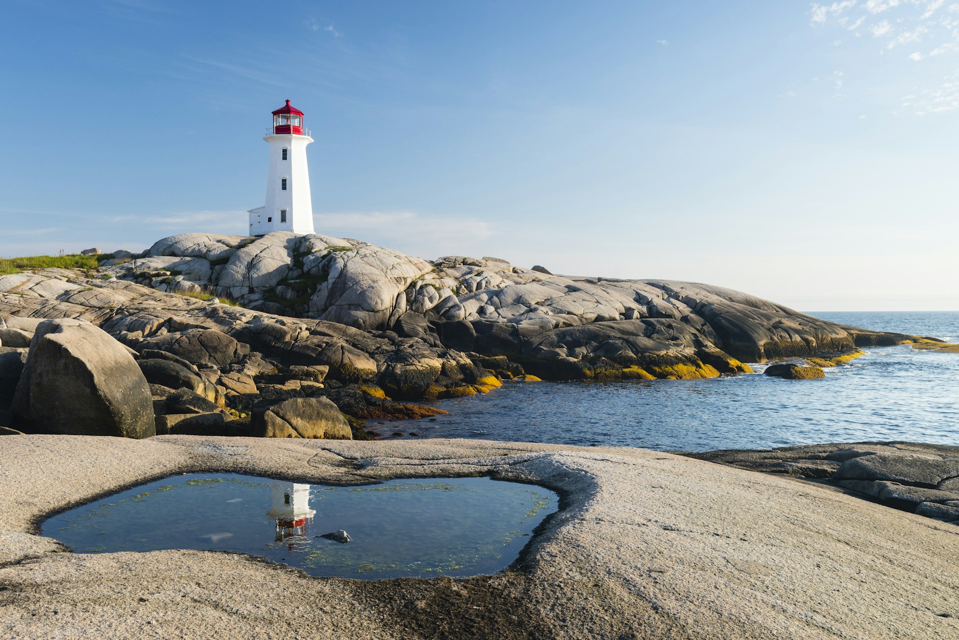 Peggy's Cove Lighthouse in Nova Scotia on a clear day, with huge boulders in front 