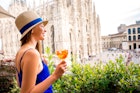 Young woman standing with traditional italian alcohol drink spritz aperol on the terrace with great view on Duomo cathedral in Milan