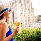 Young woman standing with traditional italian alcohol drink spritz aperol on the terrace with great view on Duomo cathedral in Milan