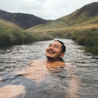 Man soaking in natural hot spring surrounded by nature in Iceland