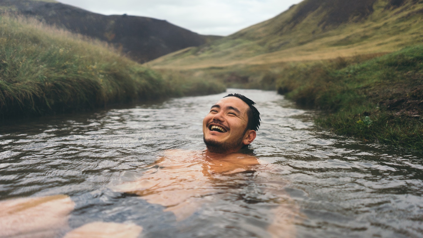Man soaking in natural hot spring surrounded by nature in Iceland
