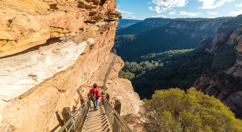 Mountain landscape with a woman hiking, going downstairs mountain track. Wentworth Falls, Blue Mountains National Park, Australia