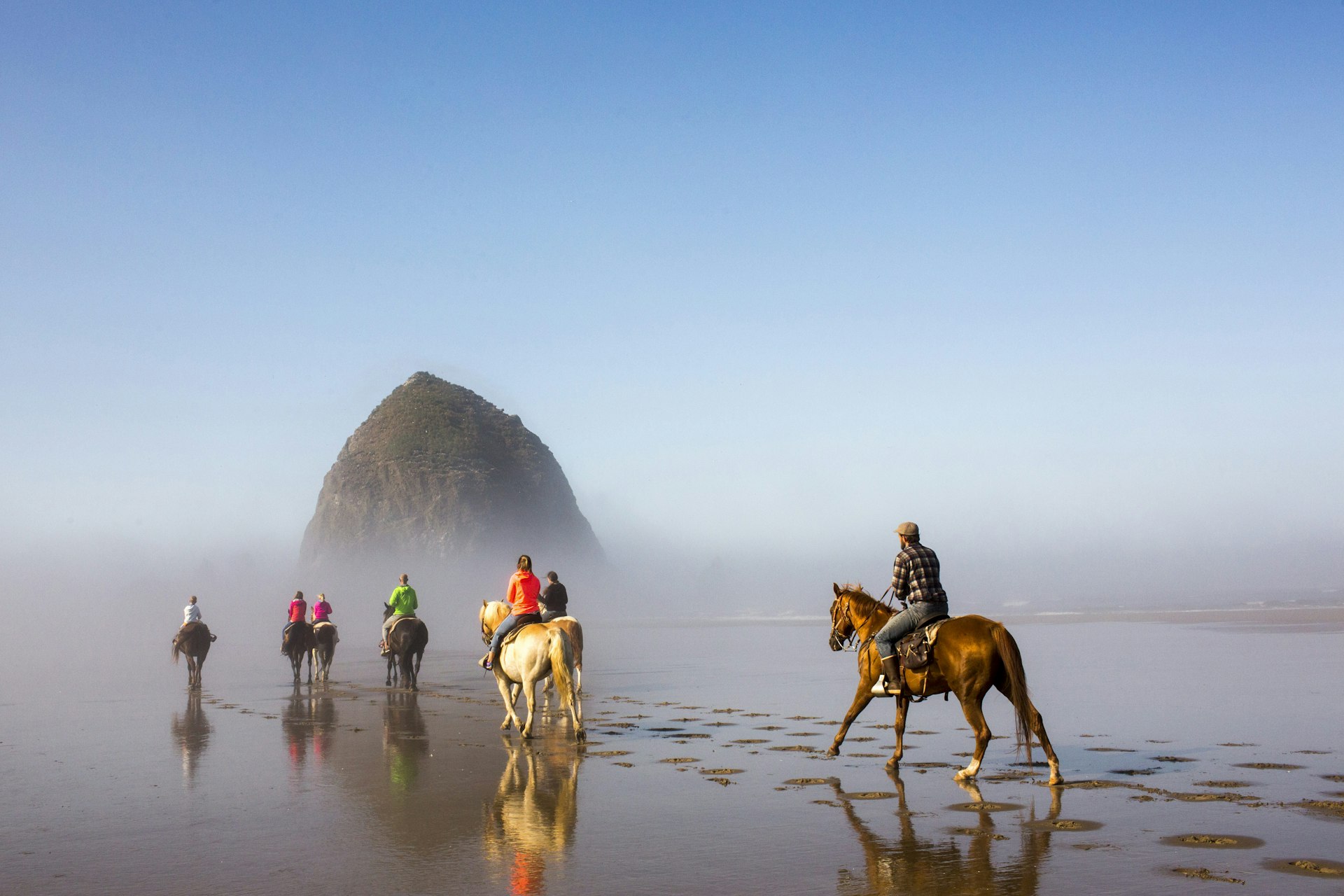 A group of people riding horses on Oregon's misty Cannon Beach. 