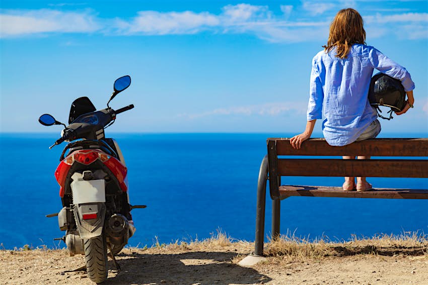 Femme avec scooter regardant l'horizon de la mer lointaine.