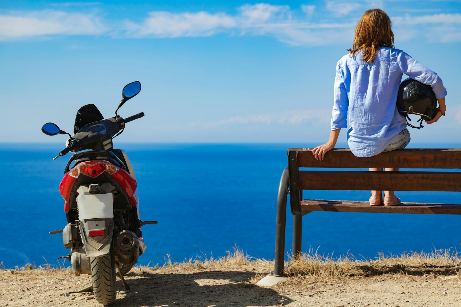 Woman with scooter looking at the distant sea horizon.