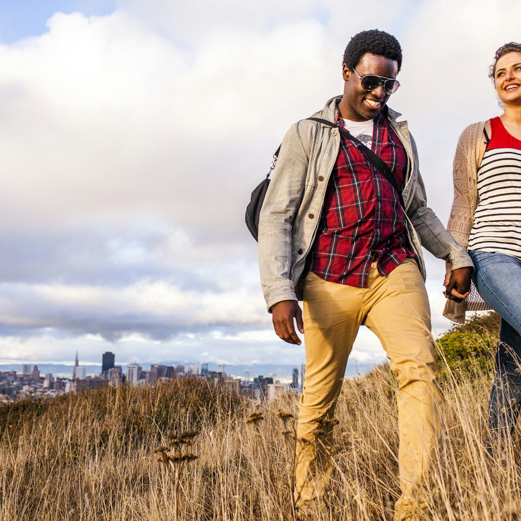 Couple walking on grassy hill overlooking cityscape