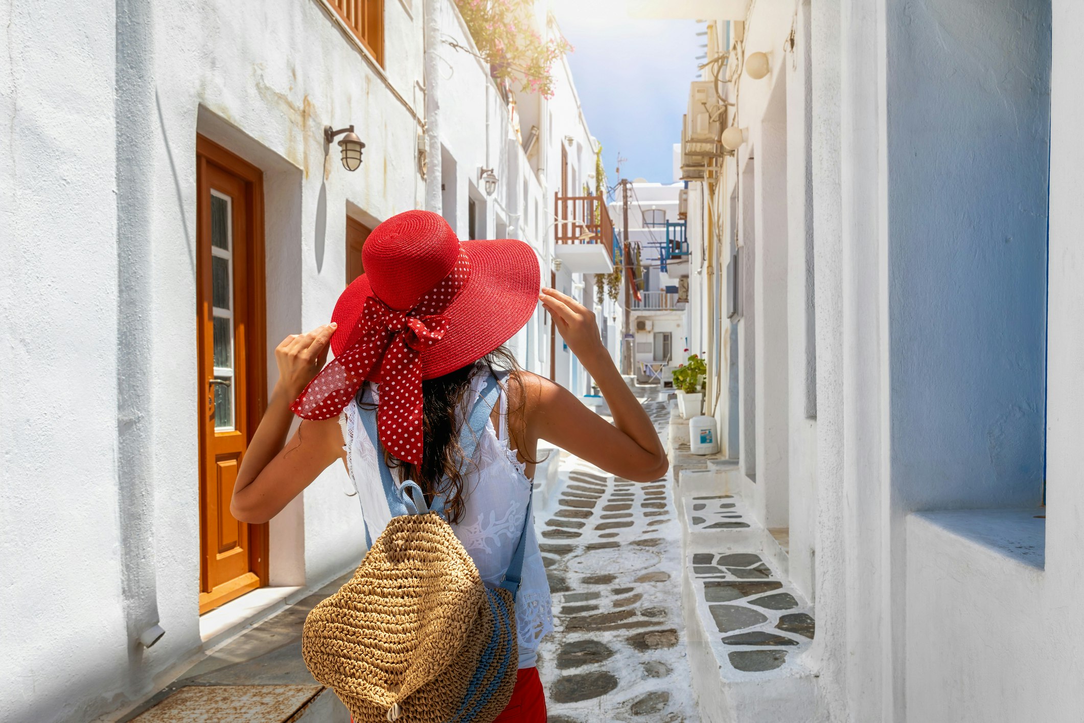 A woman wearing a large red sunhat walks through the alleys of Hora town, Mykonos