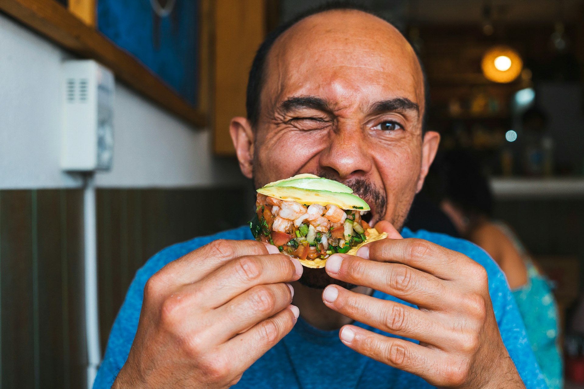 A hungry Hispanic man looking at the camera and enjoying a tasty taco