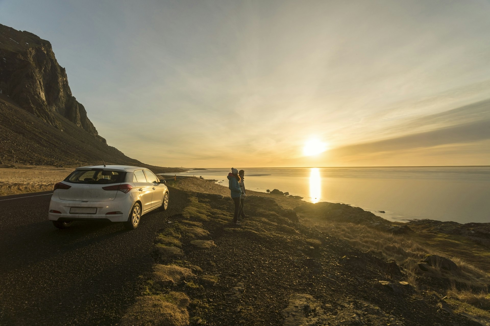 Two people stand on the side of the road next to their car, admiring the ocean view, in Stokksnes, south-eastern Iceland.
