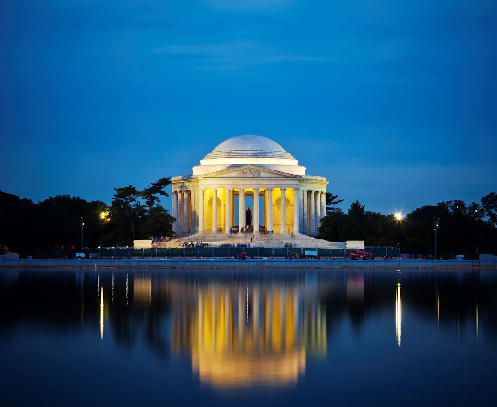 The Jefferson Memorial at night. The white-domed structure is reflected in the waters of the lake in front of it.