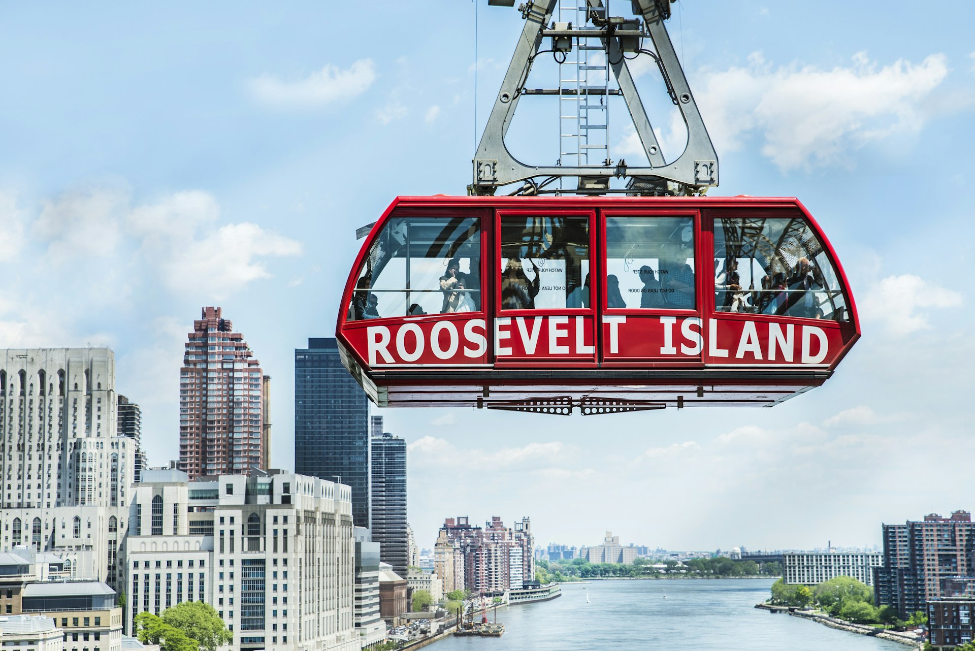 The bright-red Roosevelt Island tram suspended over the East River, with Manhattan skyscrapers gleaming in the distance