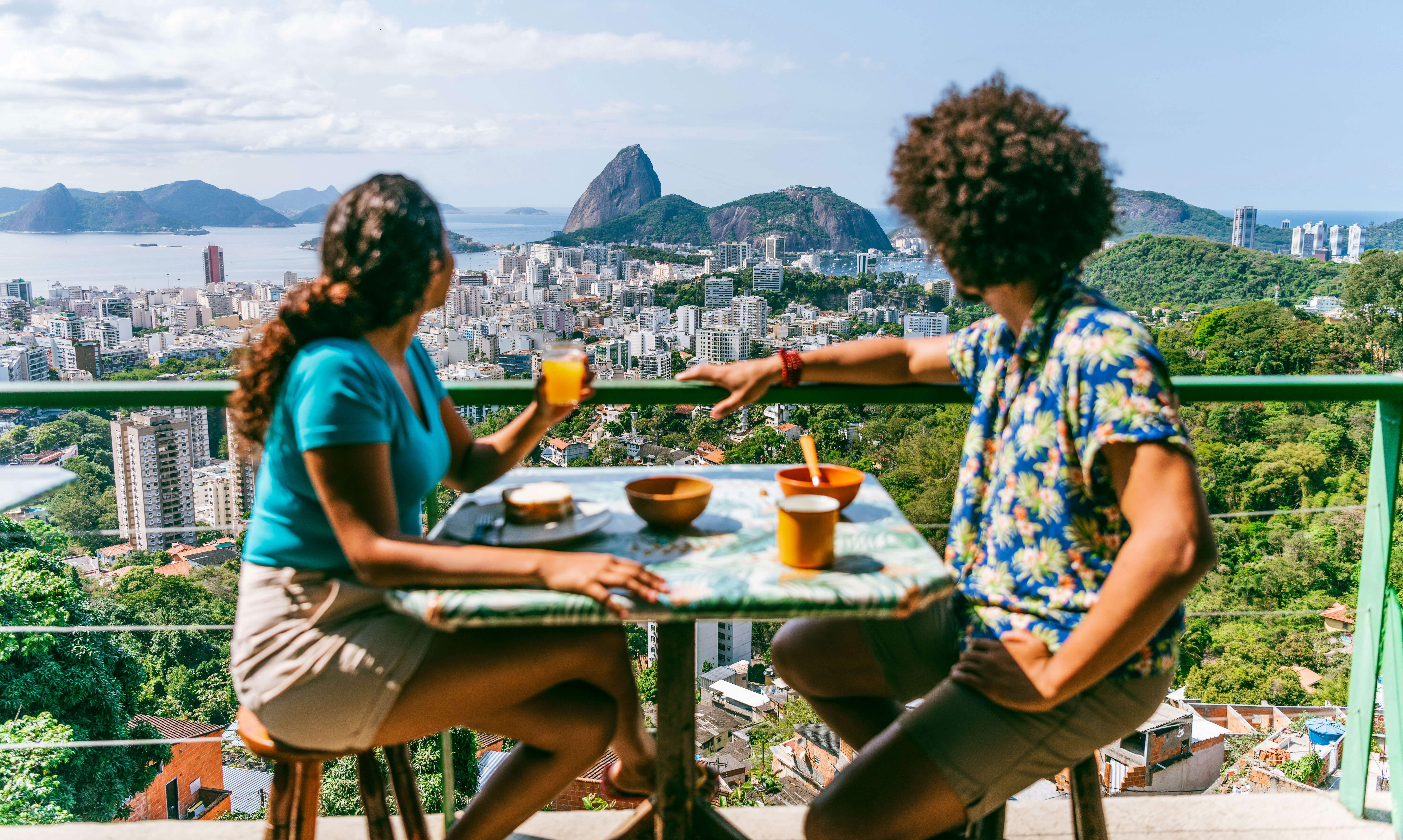Man and woman on balcony enjoying lunch, elevated view of Rio de Janeiro.