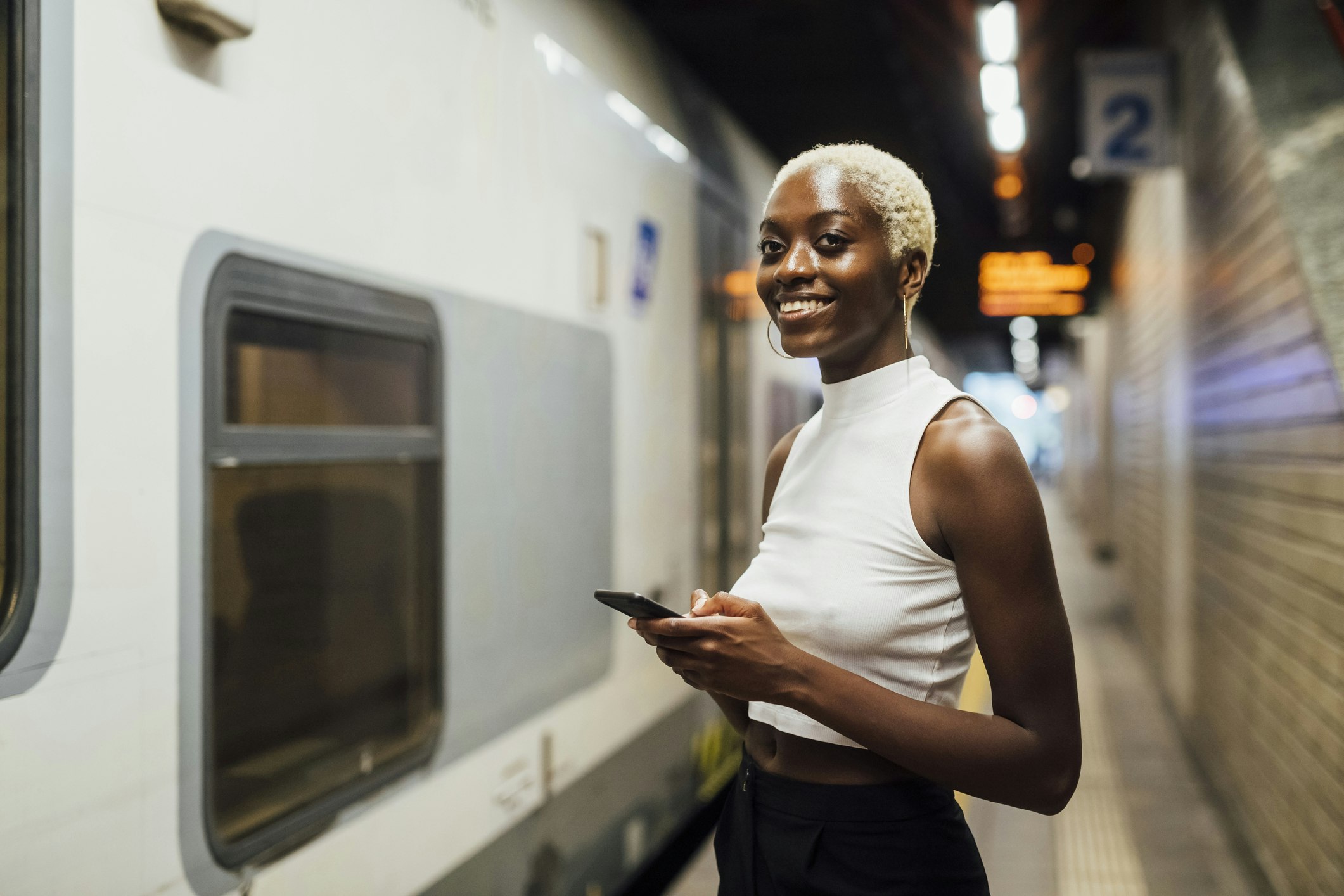 Smiling woman holding a mobile phone while standing on a subway platform