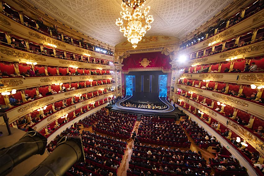 A view from the stands of the large Teatro alla Scala opera house in Milan.  The venue has lots of seating and a lit stage in the centre.