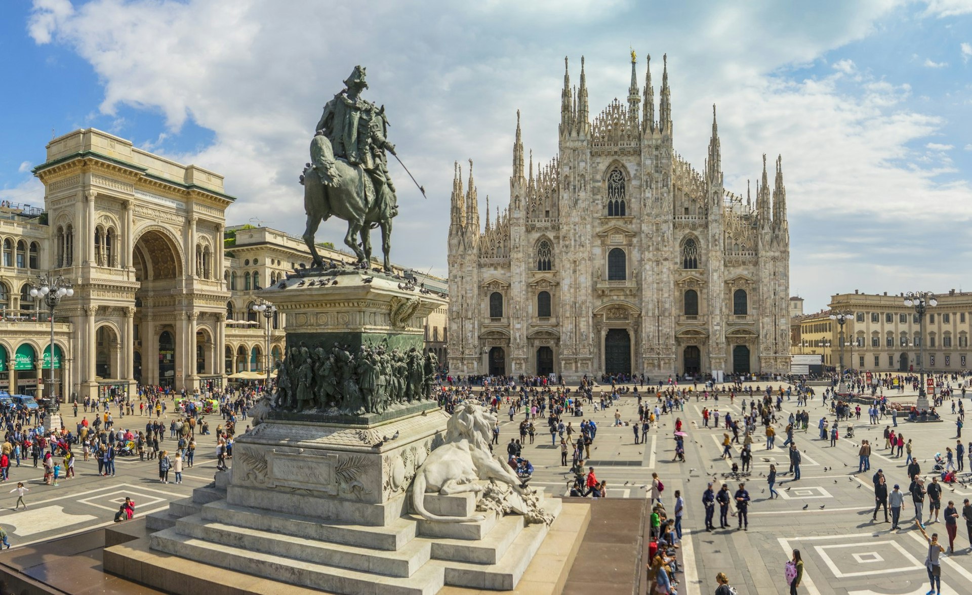 A view of the Piazza del Duomo, the Cathedral and equestrian monument to Vittorio Emanuele II in Milan. Crowds of people walk around the large square.