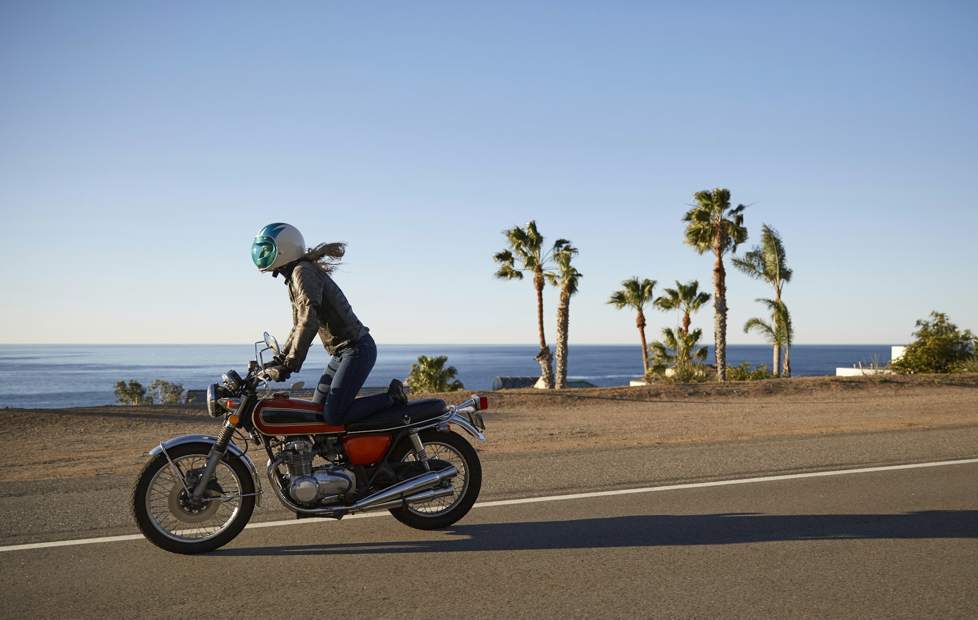Young woman riding motorcycle on empty Malibu coastline road