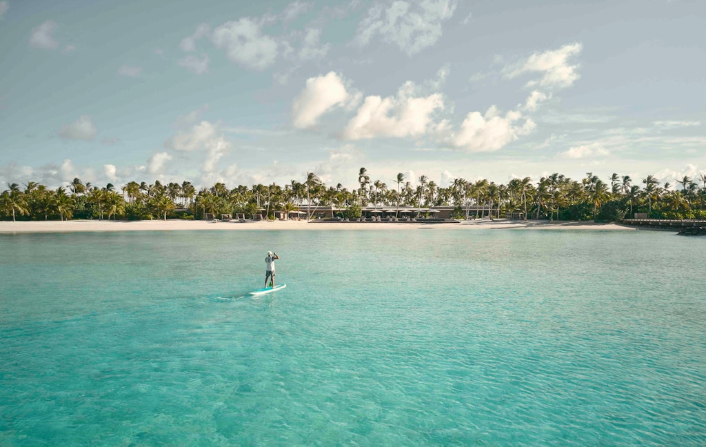 Standup paddleboarder in the turquoise waters off the shore of the Patina Maldives resort