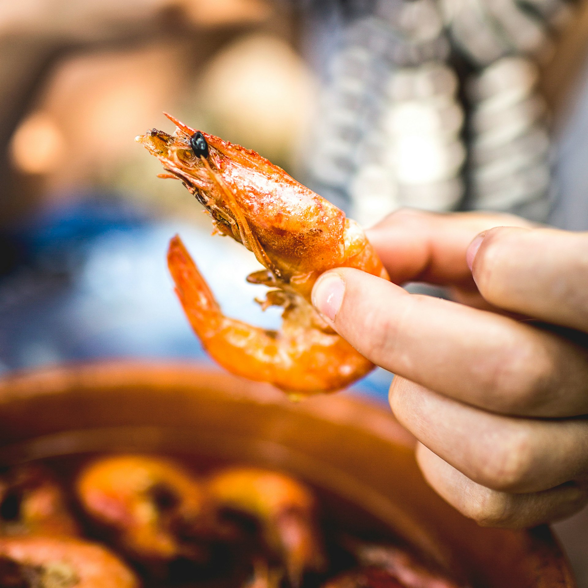 A hand holds up a shrimp cooked in garlic oil. 