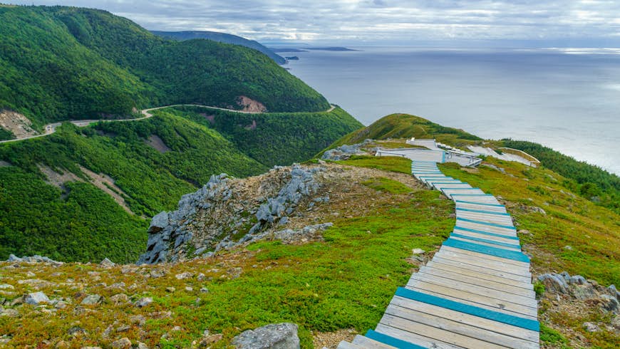 The Skyline Trail: a wooden walkway running down a green hillside in Cape Breton Highlands National Park, Canada. In the background, the sea is visible.