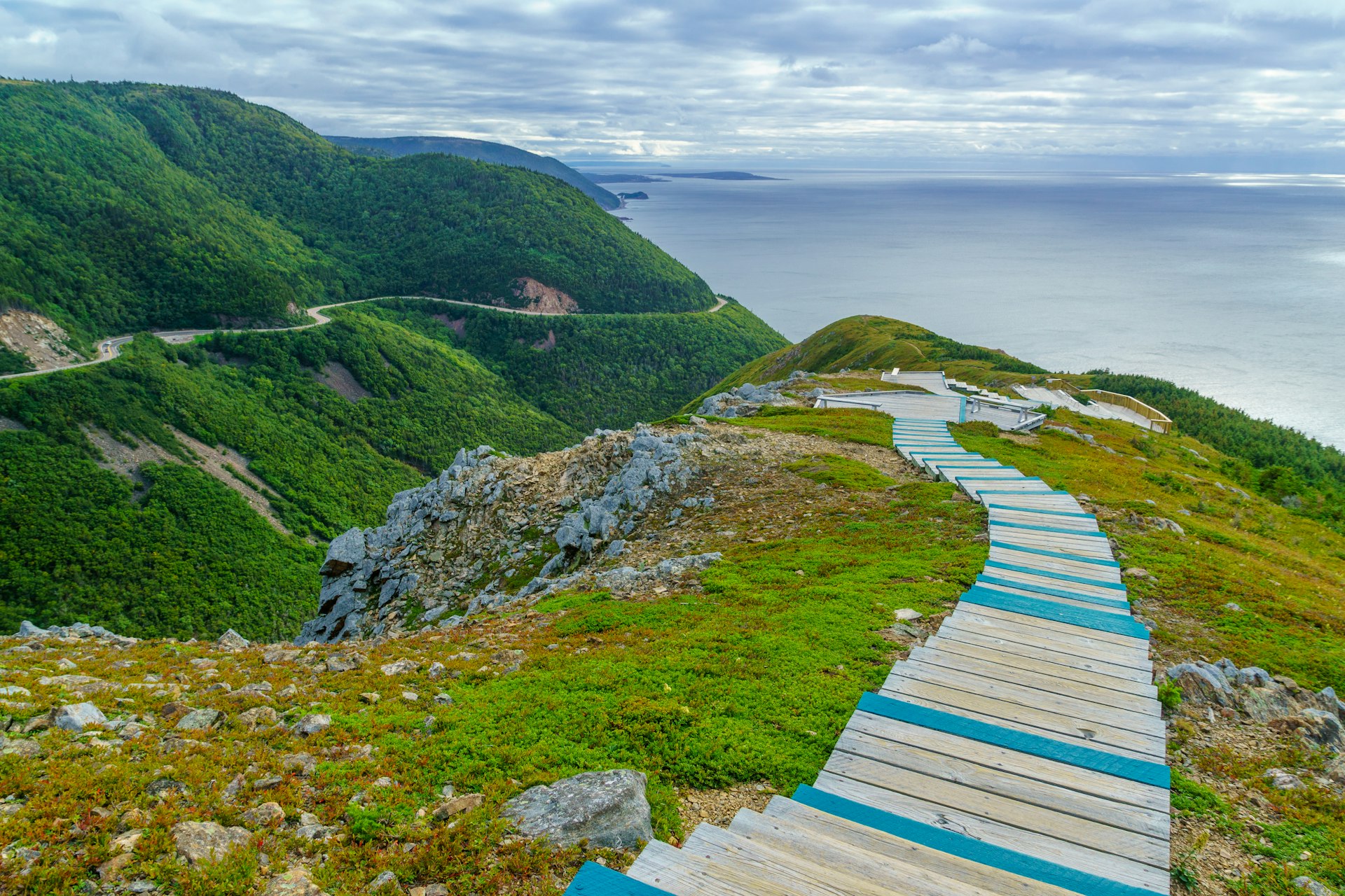 The Skyline Trail: a wooden walkway running down a green hillside in Cape Breton Highlands National Park, Canada. In the background, the sea is visible.