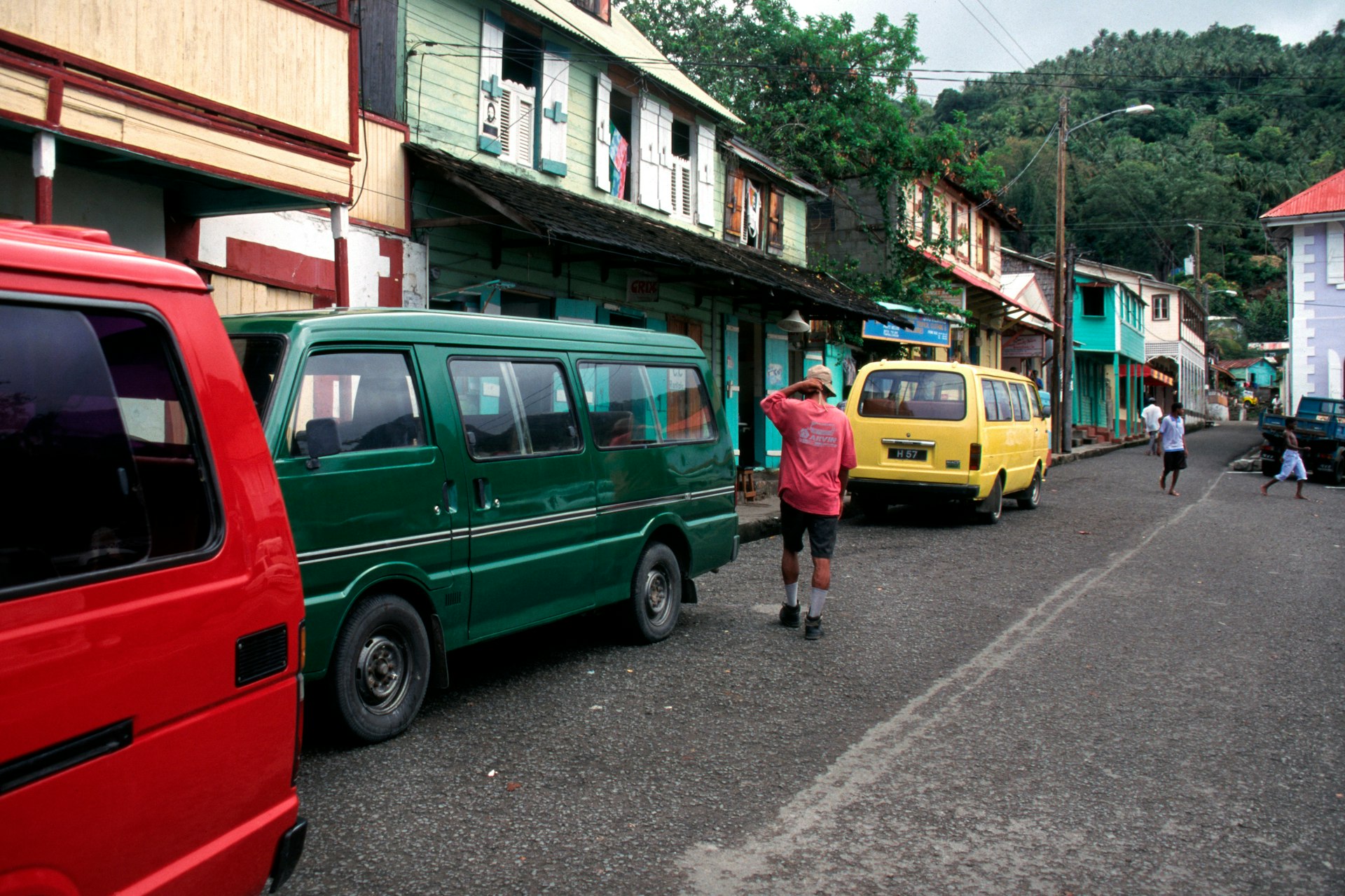 A man walks past a trio of brightly colored taxis on a busy road in St Lucia 