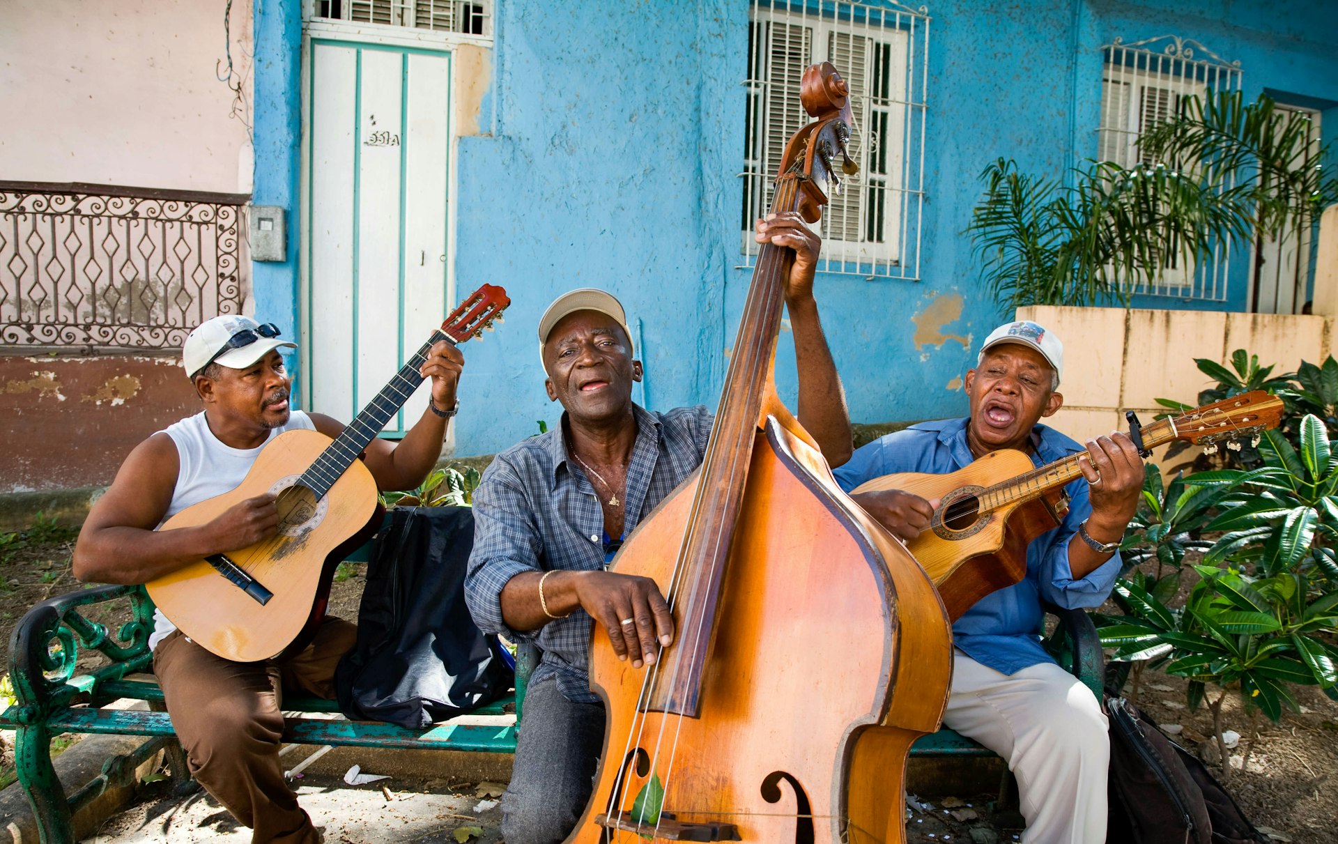 Three musicians sitting on a bench and playing music on a street in Santiago de Cuba