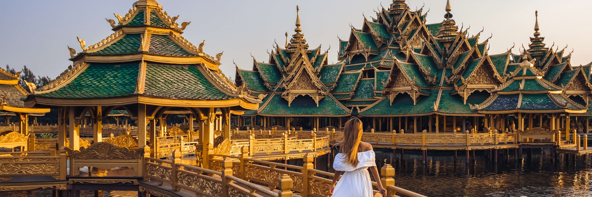 Woman walking on a bridge to Buddhist temple in Thailand during sunset.