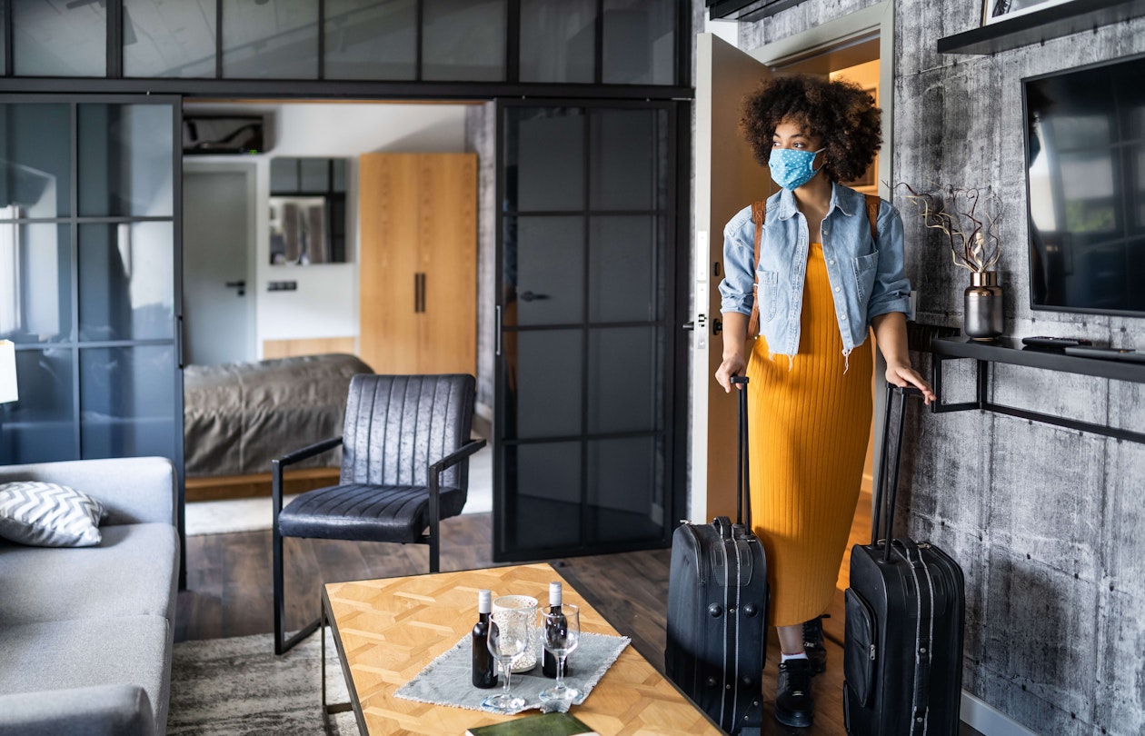 Woman with protective face mask arriving in hotel room.