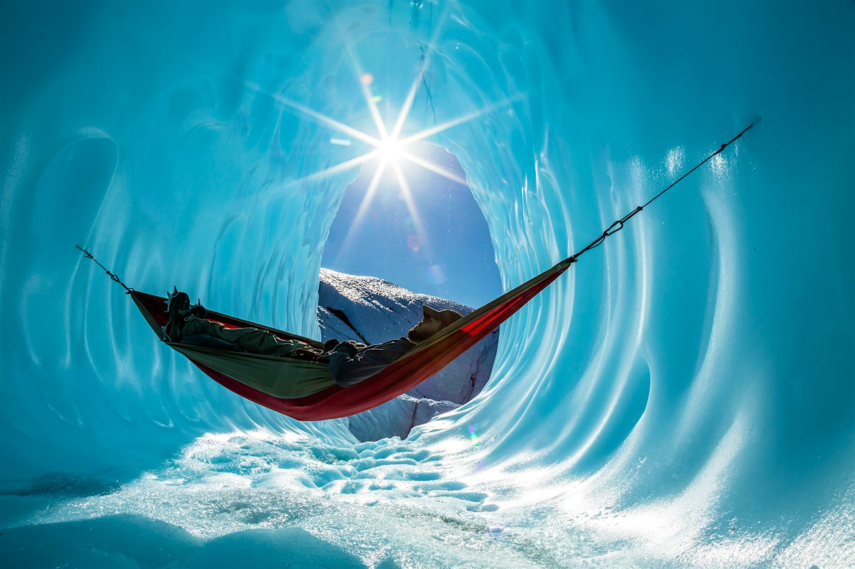 Person in hammock in ice cave with sun shining in the background