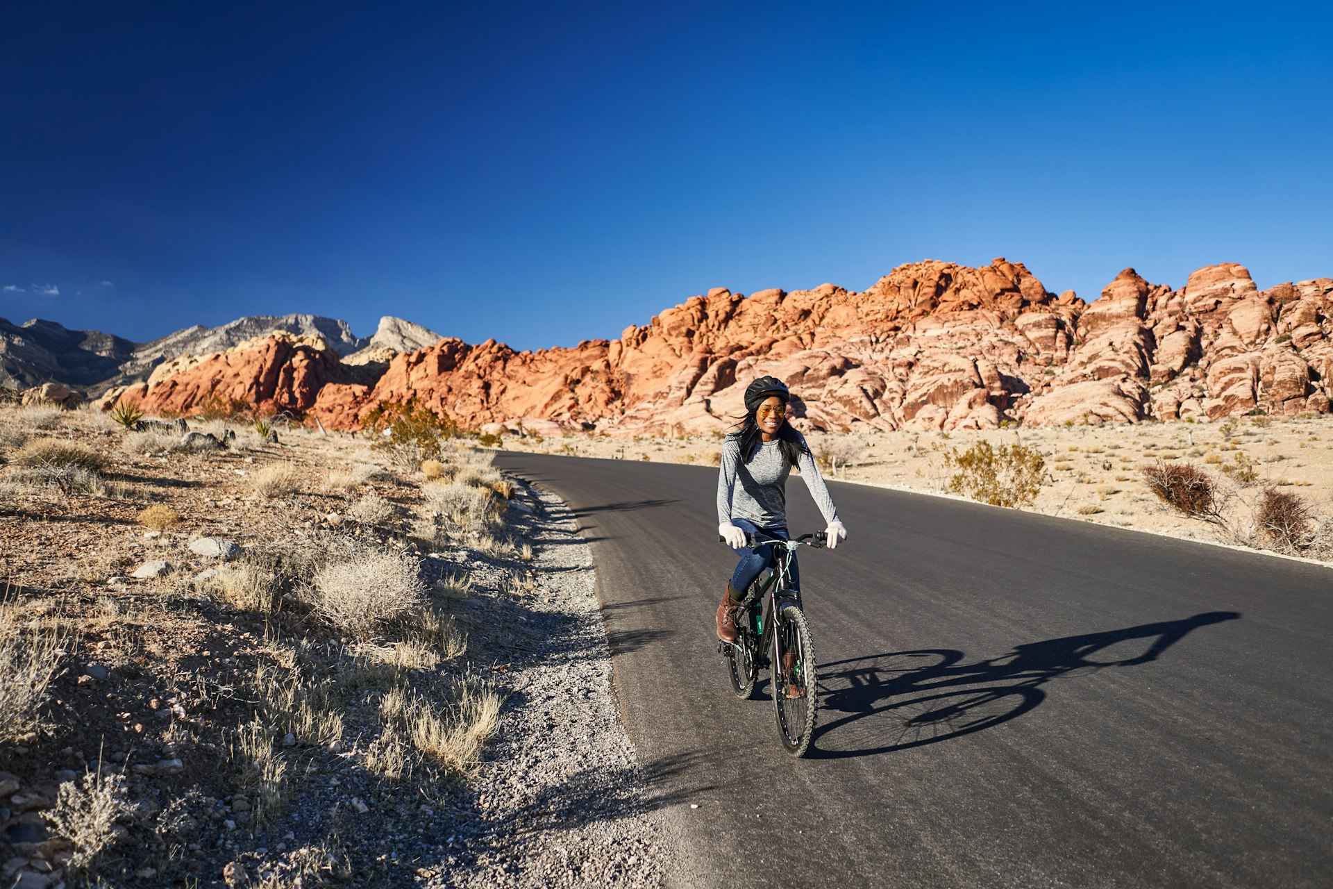 A woman cycling on a paved road through a desert landscape