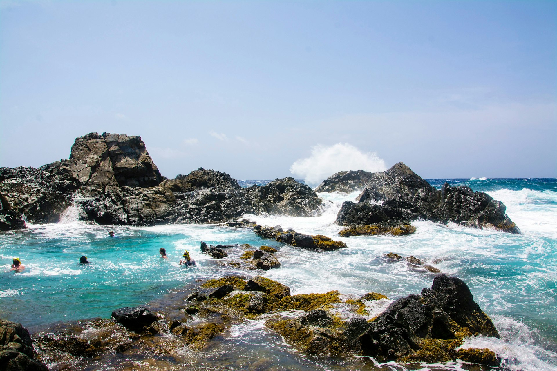 People swimming in a natural pool (conchi) by the ocean in Aruba