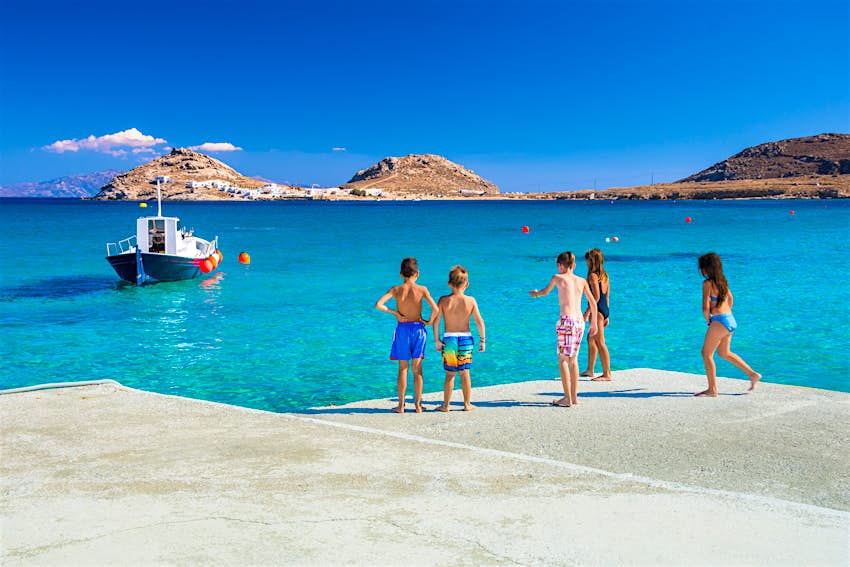 Σκάφη όλων των μεγεθών ταξιδεύουν ανάμεσα στα νησιά του Αιγαίου Ομάδα παιδιών που ετοιμάζονται να πηδήξουν στη θάλασσα από την προβλήτα στην παραλία Καλαφάτη στη Μύκονο