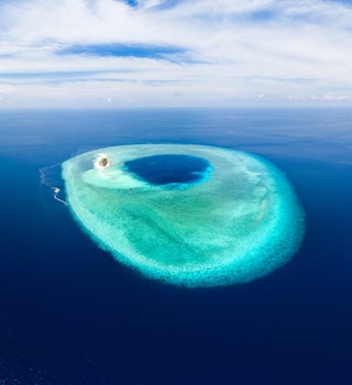Aerial of a small atoll with a blue lagoon and turquoise coral reef in Wakatobi National Park.