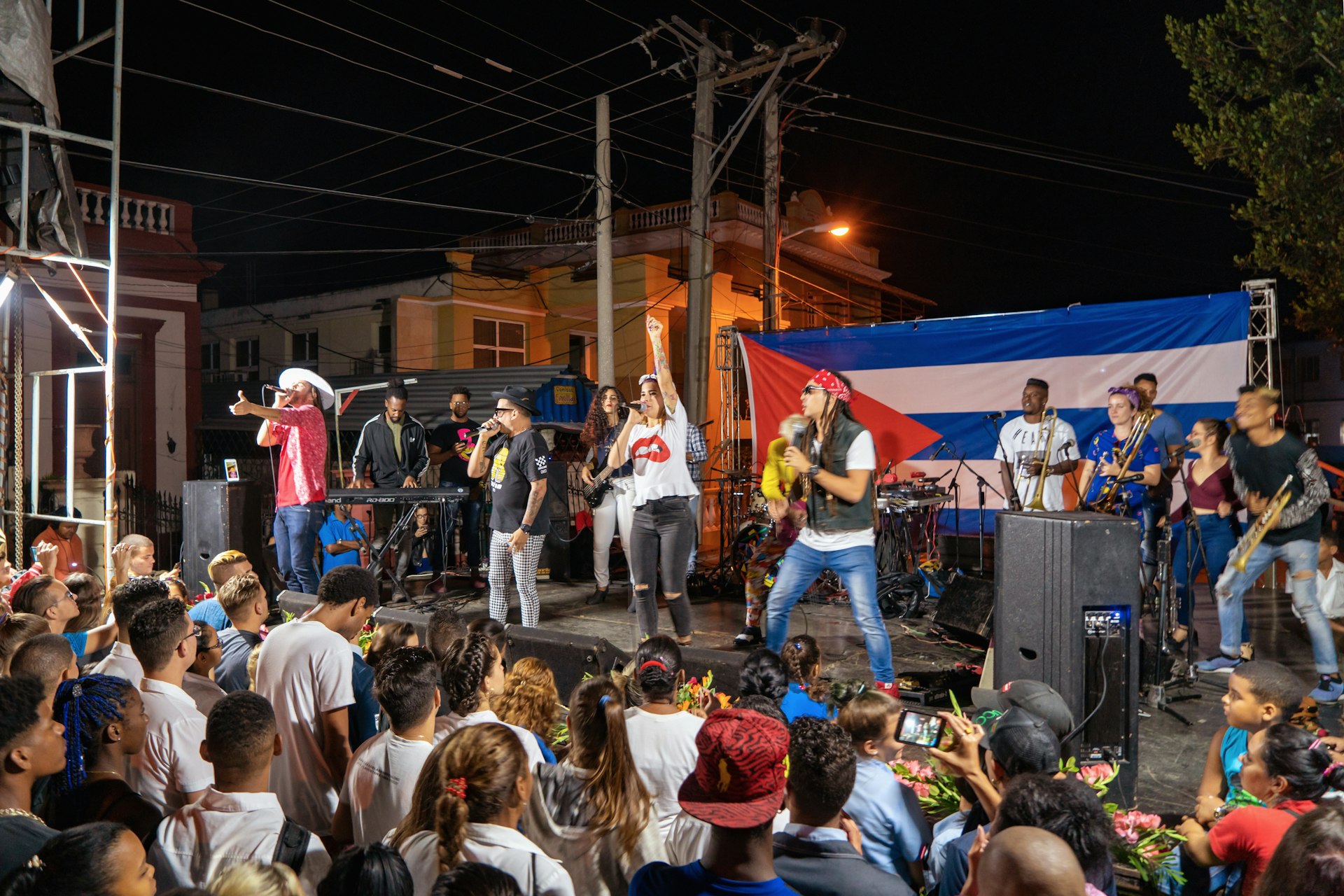 Performers on stage play to a crowd in front of a Cuban flag