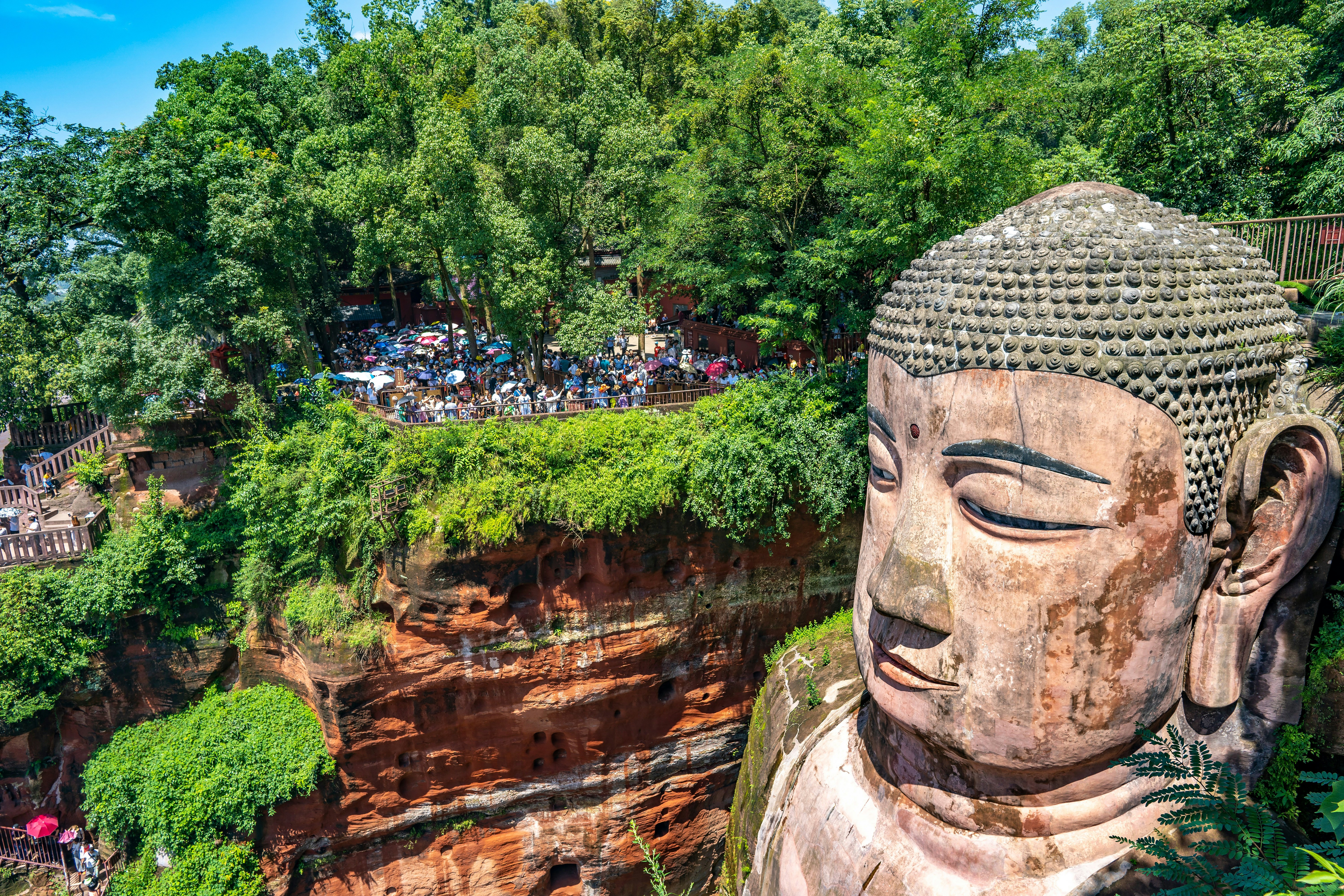 A giant stone Buddha carved into rocks. Tourists stand on a platform nearby.