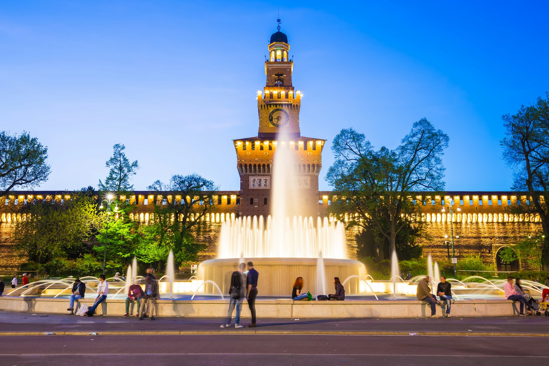 people sit around a fountain in front of Castello Sforzesco in Milan, Italy