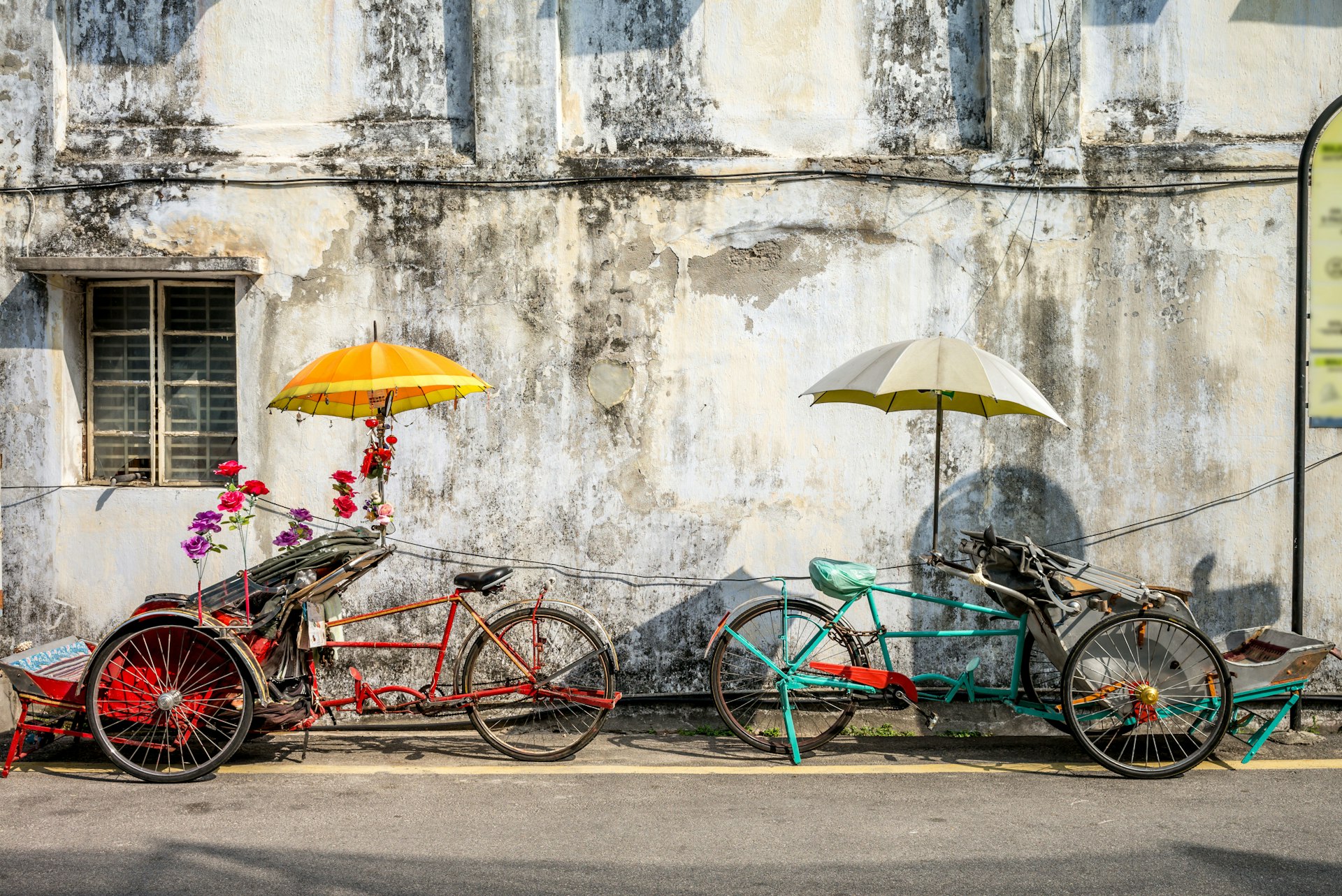 An old rickety trishaw cab parked on the sidewalk of a dilapidated building in Penang, Malaysia.