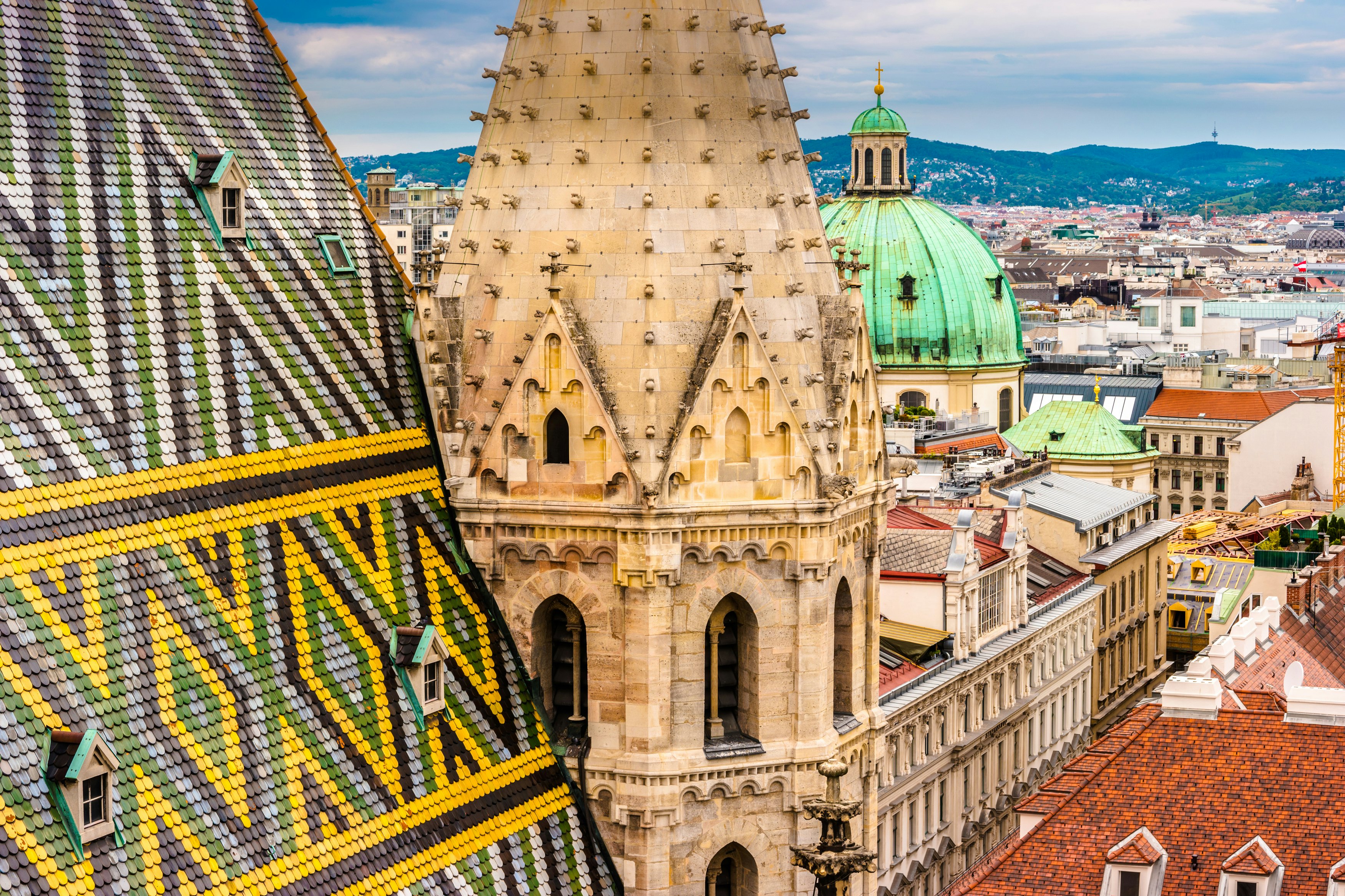 A steep church rooftop with geometric tile patterns and a Gothic cathedral spire