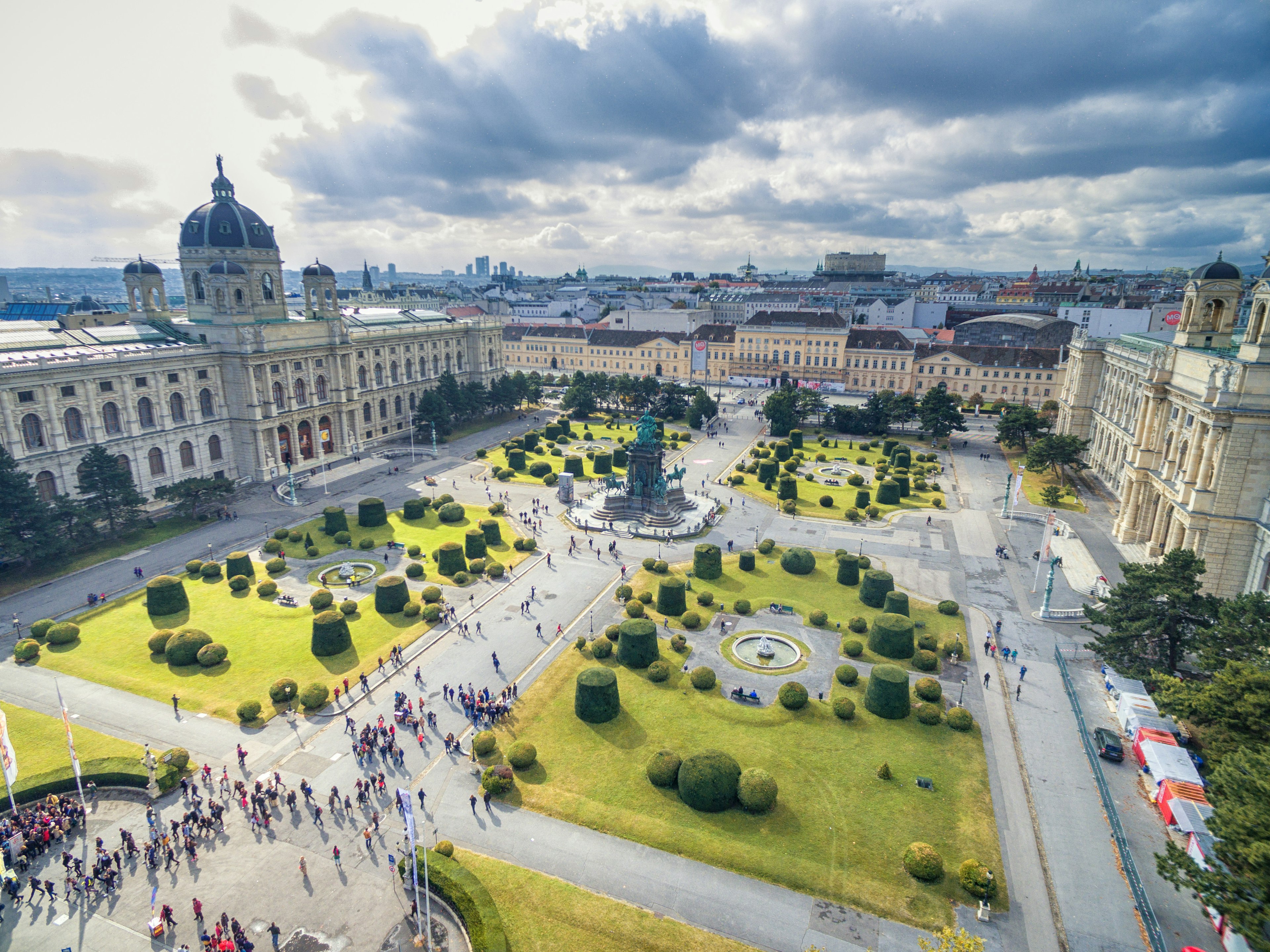 People walk around a large square with several lawns surrounded by museum buildings