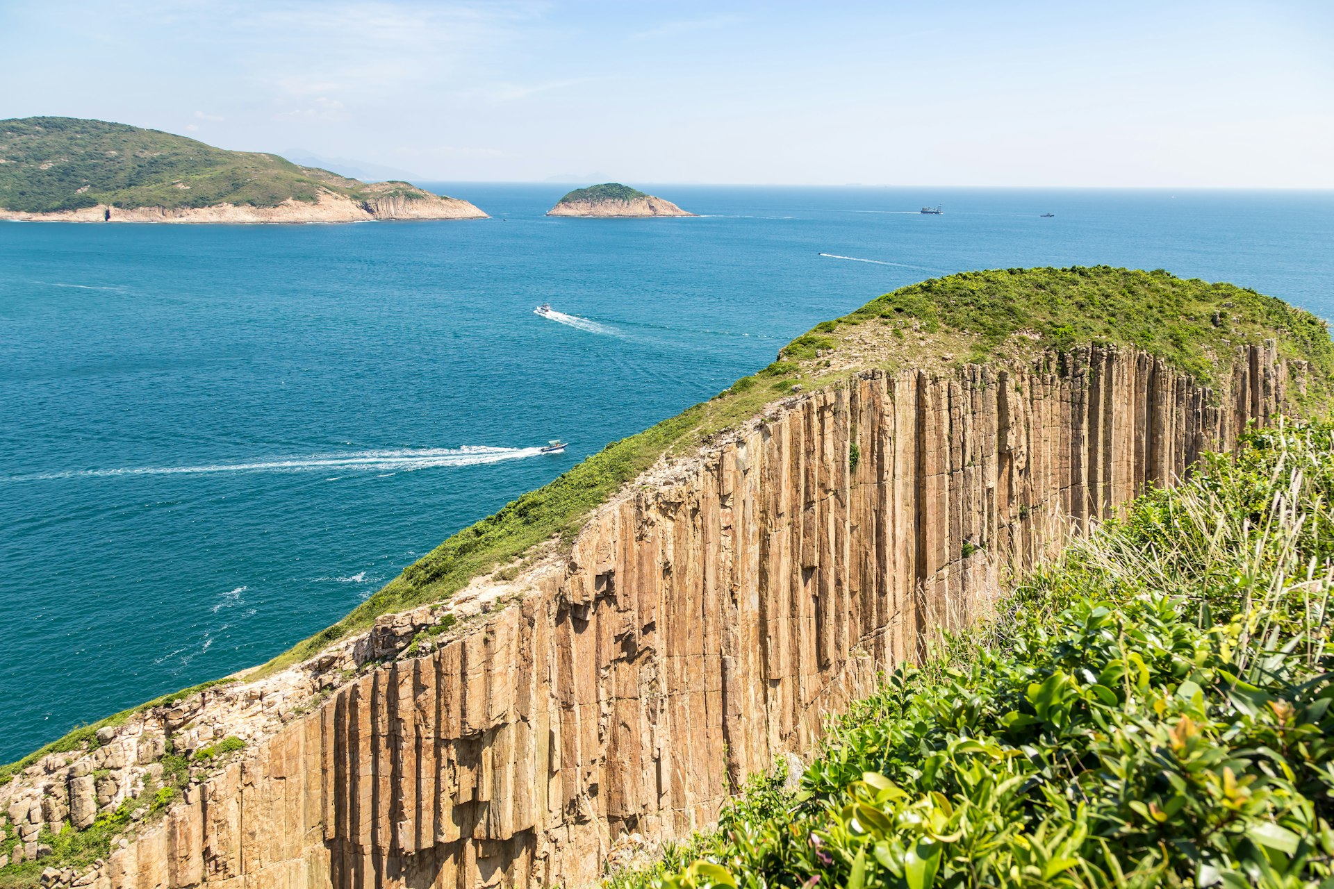 Naturally forming hexagonal rock columns on the coast of Hong Kong Geographical Park, with boats crisscrossing the ocean in the background